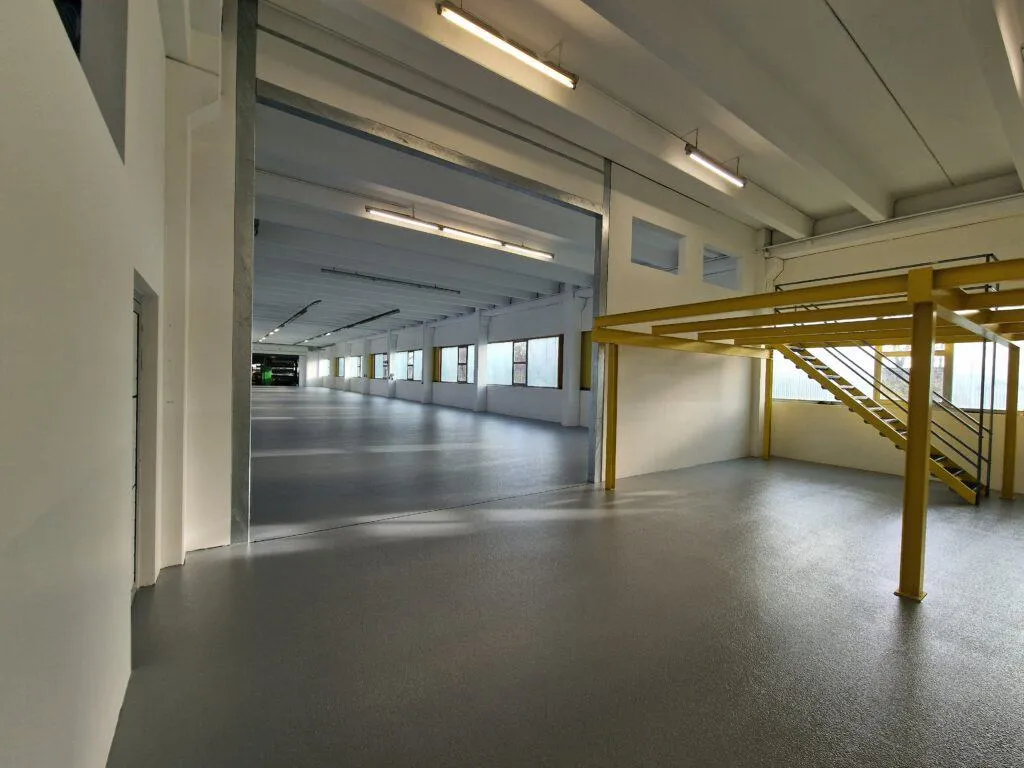 Anthrazitfarbene Bodenbeschichtung in einer Halle mit Holztreppe