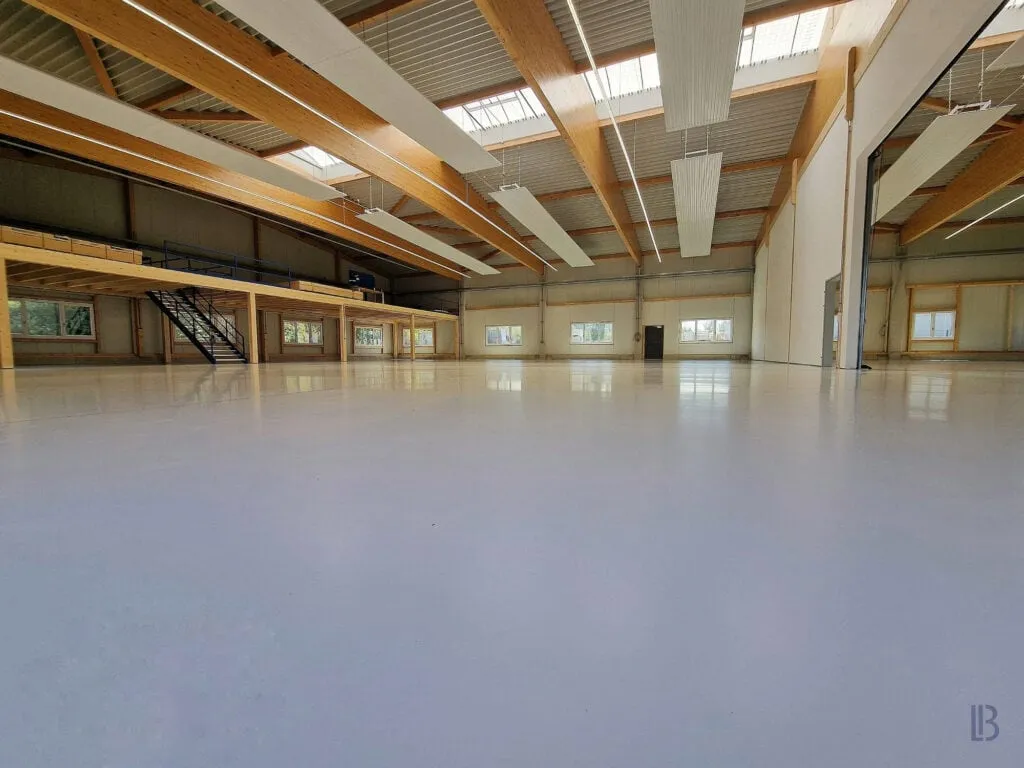 Hellgraue Bodenbeschichtung in einer Holzbauhalle mit Galerieebene